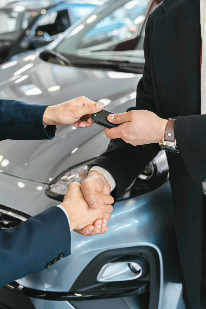 a customer and car dealer shaking hands as the customer takes a set of keys to his new car secured with an Auto Loan from Essential Credit Union