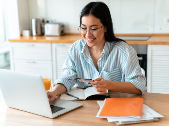 a woman smiling at her laptop while inputting her debit card information from her rewards checkign account from essential credit union in houston
