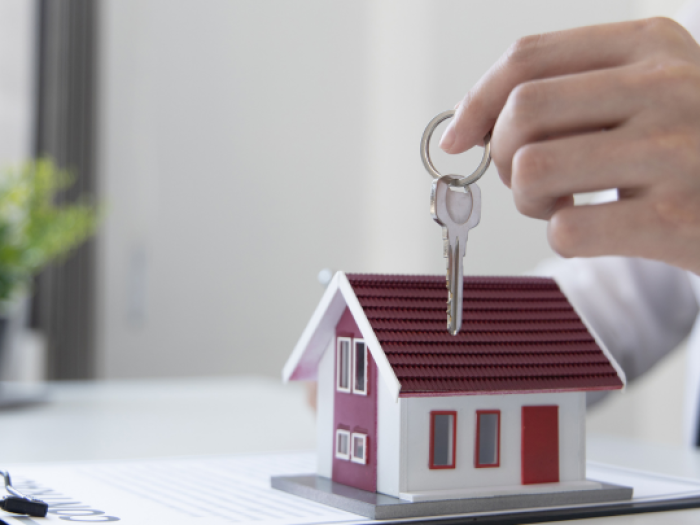 a hand holding a silver key over a small model of a white house with a red roof - home loans in gonzales
