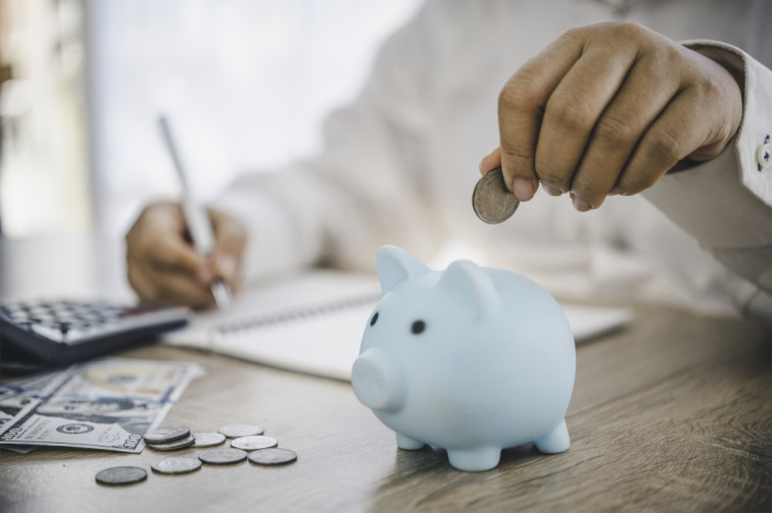 a man putting a quarter into his blue piggy bank as he calculates savings for his savings account in plaquemine