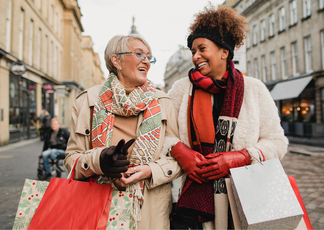 Two people in winter attire holding shopping bags on a city street.