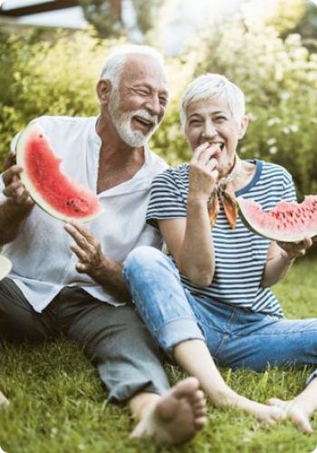 senior couple sitting on the grass in summer eating watermelon